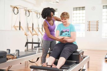 Woman starting Pilates with trainer by her side.
